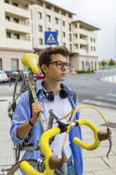 Porträt eines jungen Mannes, der ein Rennrad auf der Schulter trägt - MGIF00175