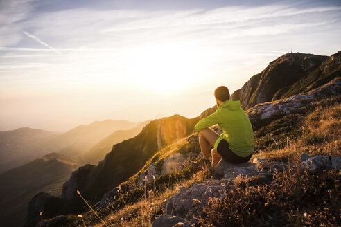 Italy, mountain running man sitting on rock looking at sunset - SIPF01790