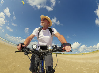 Frankreich, Bretagne, Sainte-Anne la Palud, Plage de Treguer, älterer Mann fährt Mountainbike am Strand - LAF01913