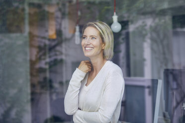 Portrait of laughing blond woman standing behind window pane - PNEF00009