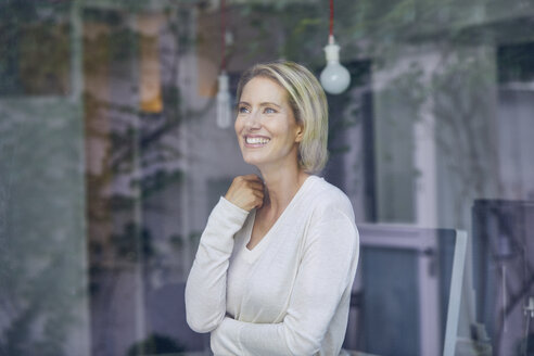 Porträt einer lachenden blonden Frau, die hinter einer Fensterscheibe steht - PNEF00009