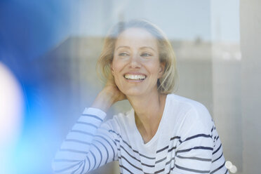 Porträt einer lachenden blonden Frau hinter einer Fensterscheibe - PNEF00017