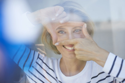 Porträt einer lachenden blonden Frau, die mit ihren Fingern einen Rahmen baut und den Betrachter ansieht, lizenzfreies Stockfoto