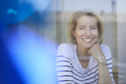 Porträt einer lachenden blonden Frau hinter einer Fensterscheibe - PNEF00019