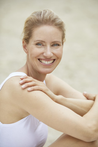 Porträt einer lachenden blonden Frau, die am Strand sitzt, lizenzfreies Stockfoto