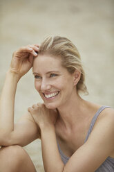 Porträt einer lachenden blonden Frau, die am Strand sitzt - PNEF00045