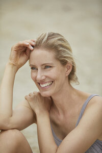 Porträt einer lachenden blonden Frau am Strand sitzend - PNEF00045