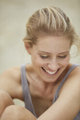 Portrait of laughing blond woman sitting on the beach - PNEF00047