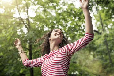 Happy young woman with raised arms dancing in nature - PNEF00051