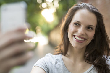 Porträt einer glücklichen jungen Frau im Freien, die ein Selfie macht - PNEF00058