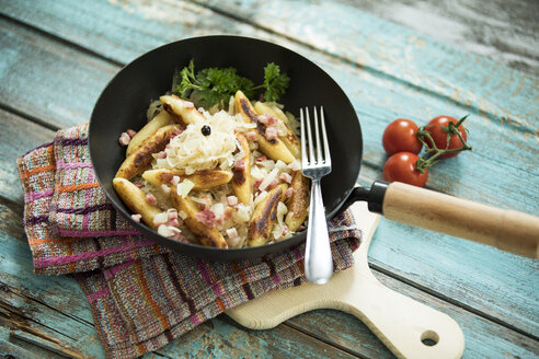 Bratpfanne mit fingerförmigen Kartoffelknödeln mit Sauerkraut und Speck auf Tuch und Holzbrett - MAEF12448