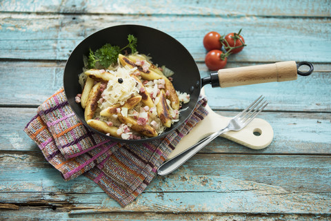 Bratpfanne mit fingerförmigen Kartoffelknödeln mit Sauerkraut und Speck auf Tuch und Holzbrett, lizenzfreies Stockfoto