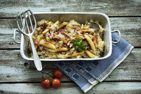 Roasting tray of finger-shaped potato dumplings with sauerkraut and bacon on cloth and wood - MAEF12453