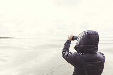 Niederlande, Ouddorp, Rückenansicht einer Frau, die im Herbst ein Selfie am Strand macht - CHPF00436