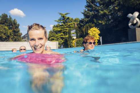 Portrait of happy woman with group of seniors swimimng in swimming pool - PNPF00111