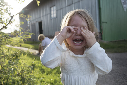 Porträt eines schreienden kleinen Mädchens, das seine Augen mit den Händen bedeckt - KMKF00016