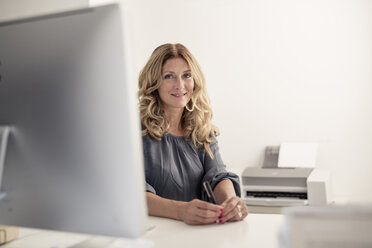 Portrait of smiling businesswoman at desk in office - PNEF00077