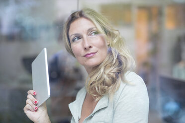 Businesswoman holding tablet behind windowpane - PNEF00087