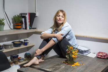 Blond woman at home sitting on wooden table - PNEF00106