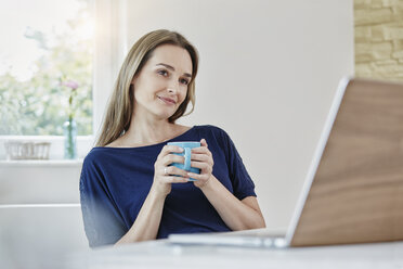 Frau zu Hause mit Kaffeetasse und Laptop - RORF01021