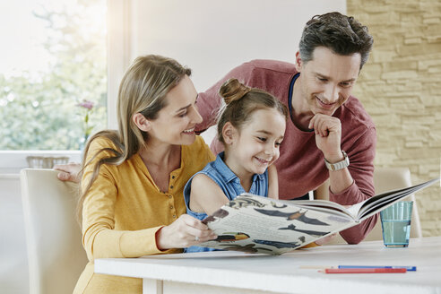 Glückliche Familie zu Hause beim Betrachten eines Bilderbuchs - RORF01024
