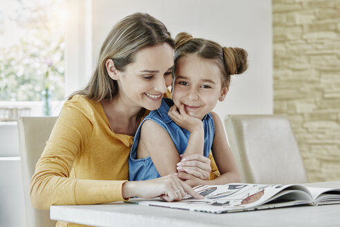Glückliche Mutter mit Tochter zu Hause beim Betrachten eines Bilderbuchs - RORF01028