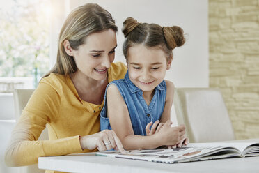 Happy mother with daughter at home looking at picture book - RORF01031