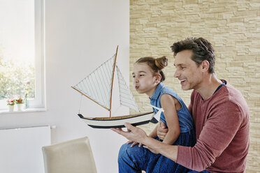 Glücklicher Vater und Tochter spielen zu Hause mit einem Modellboot - RORF01034