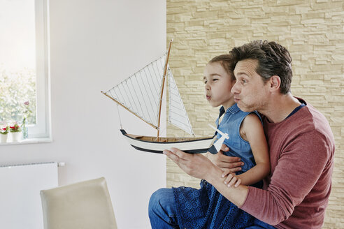 Glücklicher Vater und Tochter spielen zu Hause mit einem Modellboot - RORF01035