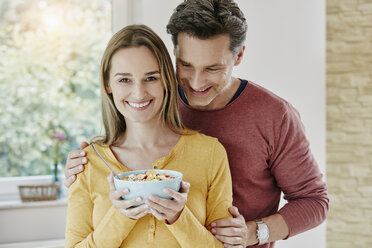 Happy couple holding bowl with muesli at home - RORF01038