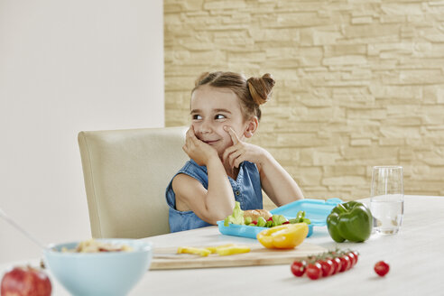 Lächelndes Mädchen am Tisch, das eine Lunchbox mit gesunden Lebensmitteln packt - RORF01040