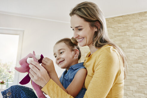 Glückliche Mutter und Tochter spielen mit Kuscheltier zu Hause - RORF01041