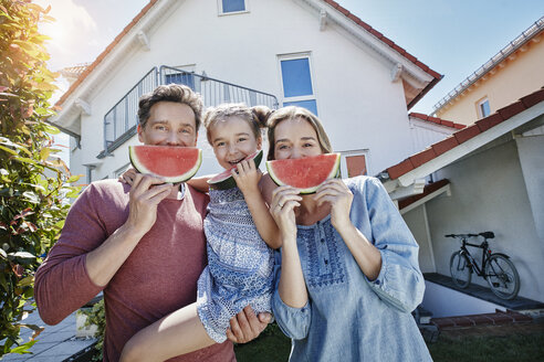 Porträt einer glücklichen Familie mit Scheiben von Wassermelone vor ihrem Haus - RORF01045