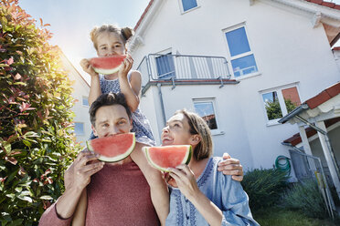 Porträt einer glücklichen Familie mit Scheiben von Wassermelone vor ihrem Haus - RORF01046