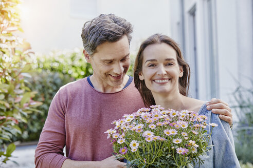 Porträt eines lächelnden Paares mit Blumen vor ihrem Haus - RORF01048