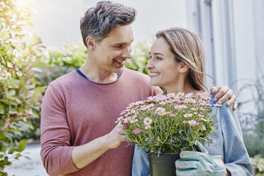 Lächelndes Paar mit Blumen vor ihrem Haus - RORF01049