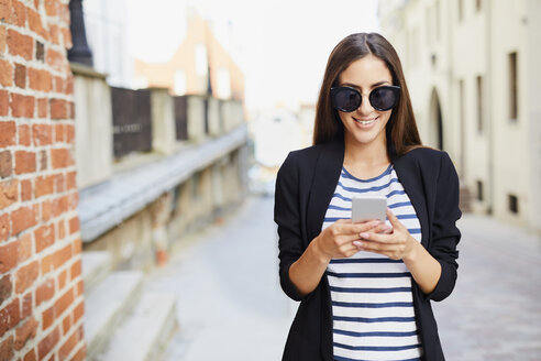 Young woman wearing sunglasses using phone outdoors - BSZF00064