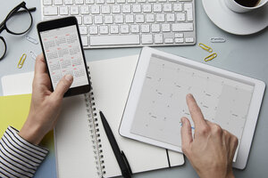 Top view of woman holding smartphone and tablet with calendar on desk - RBF06096
