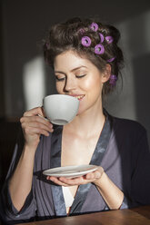 Junge Frau mit Lockenwicklern trinkt eine Tasse Kaffee - PNEF00117