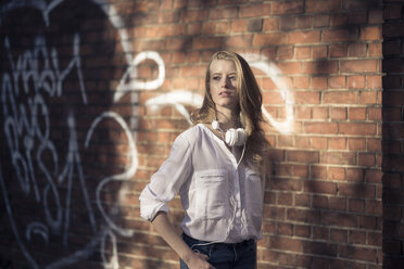 Portrait of young woman with headphones in front of brick wall - PNEF00121