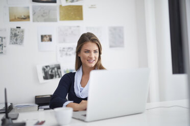 Lächelnde junge Frau mit Laptop am Schreibtisch im Büro - PNEF00136