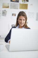 Smiling young woman using laptop at desk in office - PNEF00137