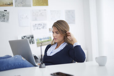 Young woman using laptop at desk in office - PNEF00138