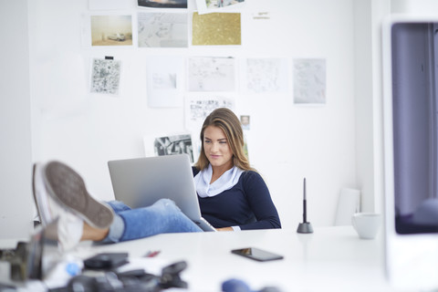 Smiling young woman using laptop at desk in office stock photo