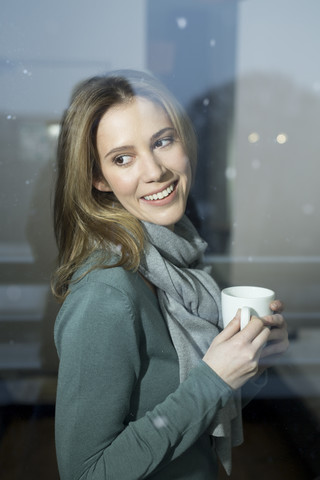 Smiling woman holding cup looking out of window stock photo