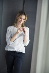 Smiling woman holding glass of water at the window - PNEF00152