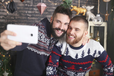 Porträt eines glücklichen schwulen Paares, das zu Weihnachten zu Hause ein Selfie mit dem Smartphone macht - RTBF01036