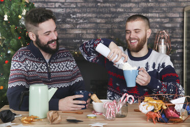 Schwules Paar bei der Zubereitung von heißer Schokolade mit Sahne und gehackten Zuckerstangen zur Weihnachtszeit - RTBF01038