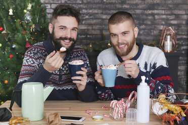 Glückliches schwules Paar trinkt heiße Schokolade mit Sahne und gehackten Zuckerstangen zur Weihnachtszeit - RTBF01040