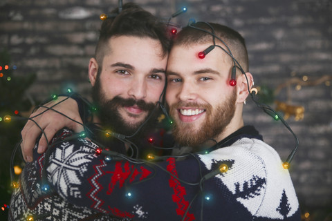 Porträt eines glücklichen schwulen Paares mit Lichterkette zur Weihnachtszeit, lizenzfreies Stockfoto